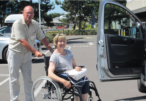 Man helping a lady to get into a car the lady is sat in a wheelchair